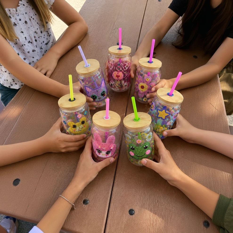 bedazzle workshop Six colorful handmade bead and glitter tumblers are arranged in a circle on a wooden picnic table.