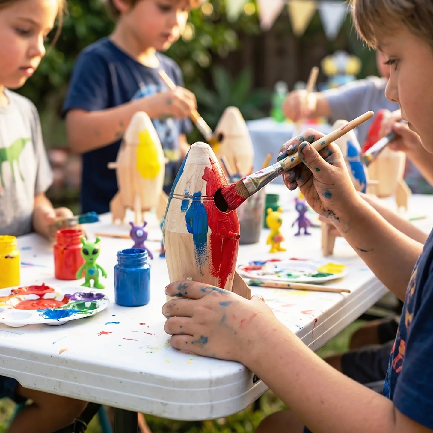Children painting wooden figures at a table outdoors in Los Angeles. Creative birthday party craft activity with DIY wooden toys.
