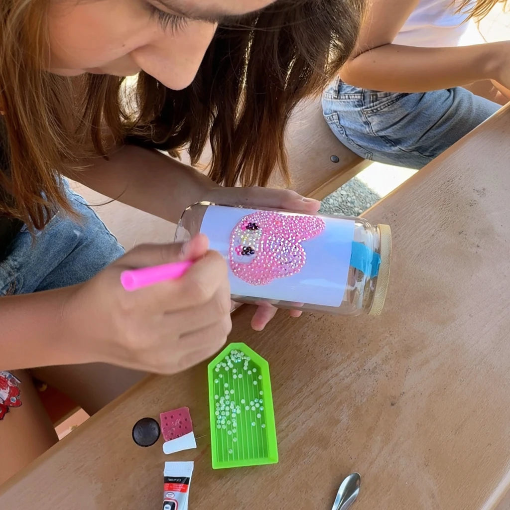 girl placing gems on personalized glass treasure jars during a birthday party craft activity.