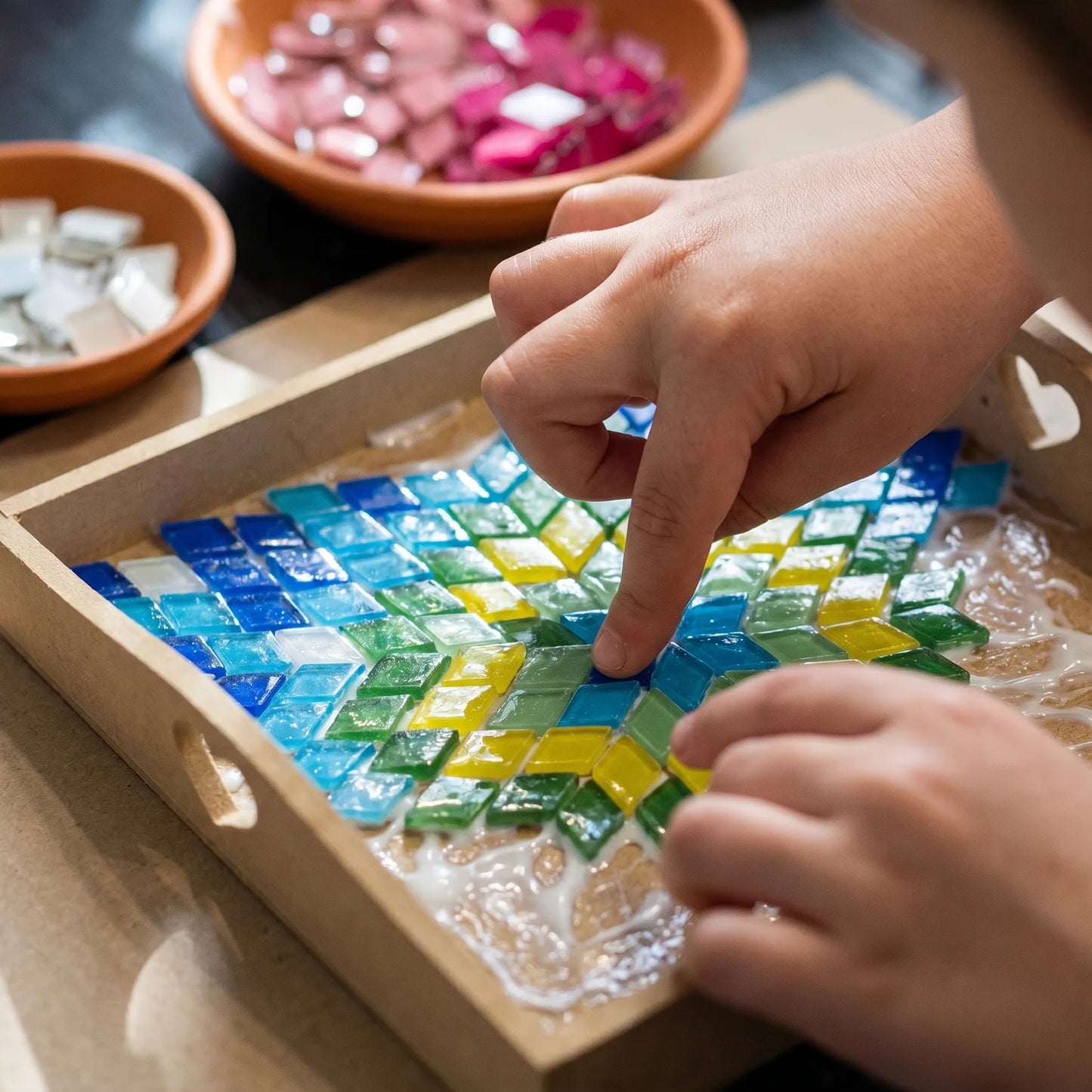 Children's hands working on a colorful glass mosaic art project during a hands-on craft workshop in Los Angeles 