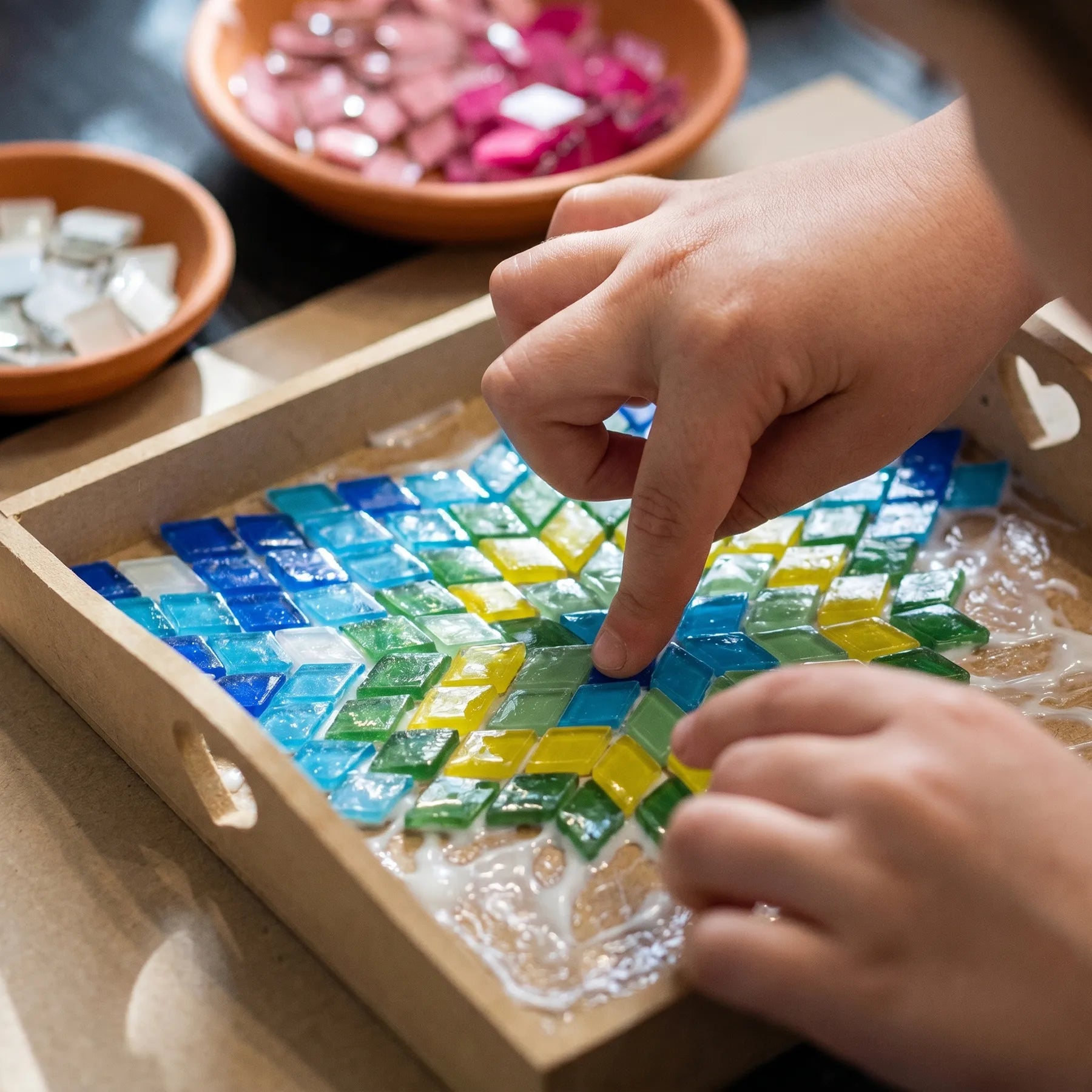 Children's hands working on a colorful glass mosaic art project during a hands-on craft workshop in Los Angeles 