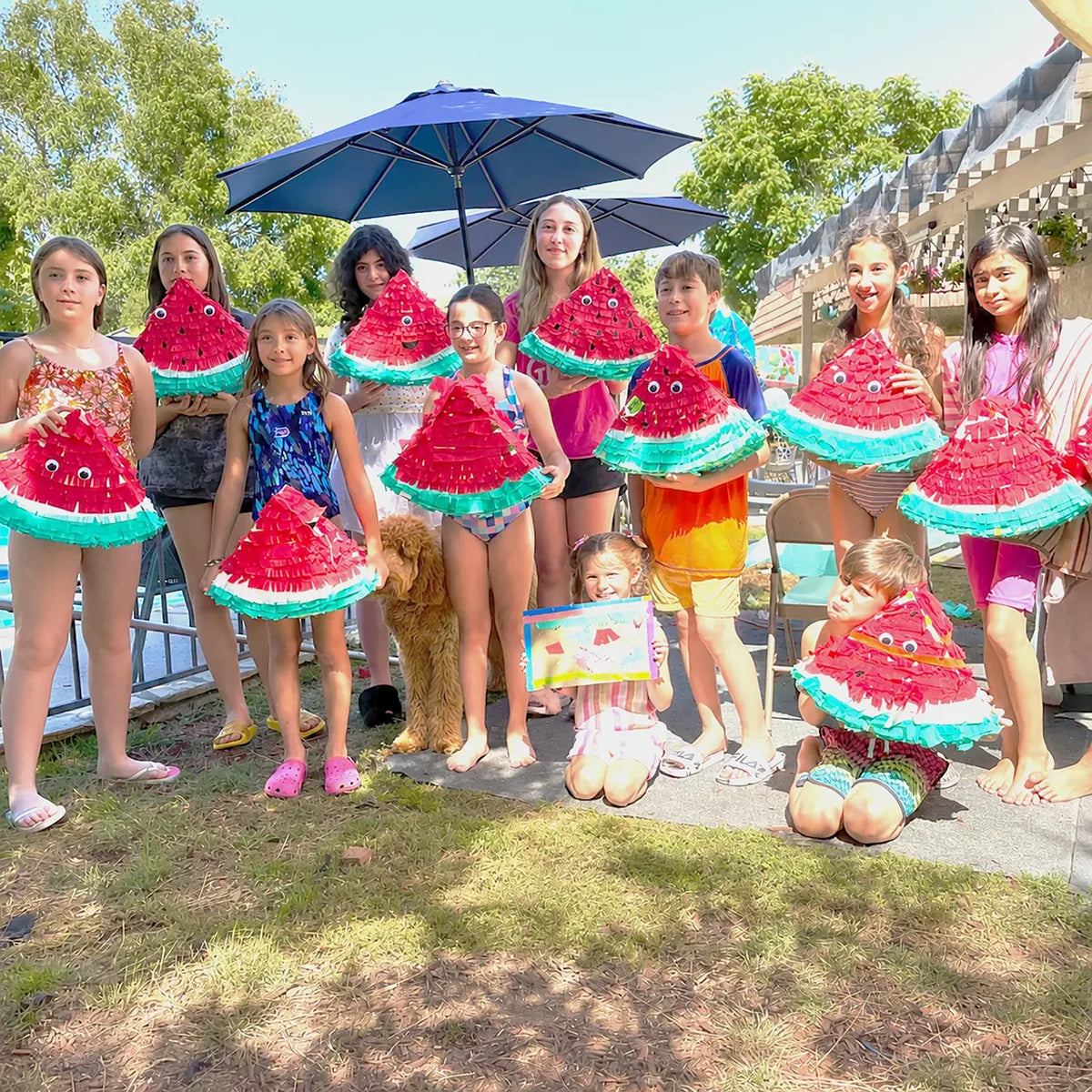 Group of children holding handmade watermelon piñata crafts during an outdoor birthday party workshop in Los Angeles